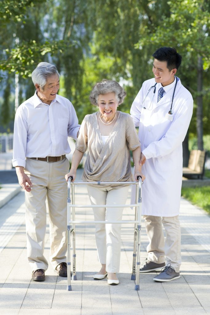 Senior woman walking with walking frame under doctor and husband's assistance