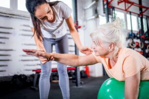 Senior woman with trainer doing rehab using pilates ball in the rehabilitation center